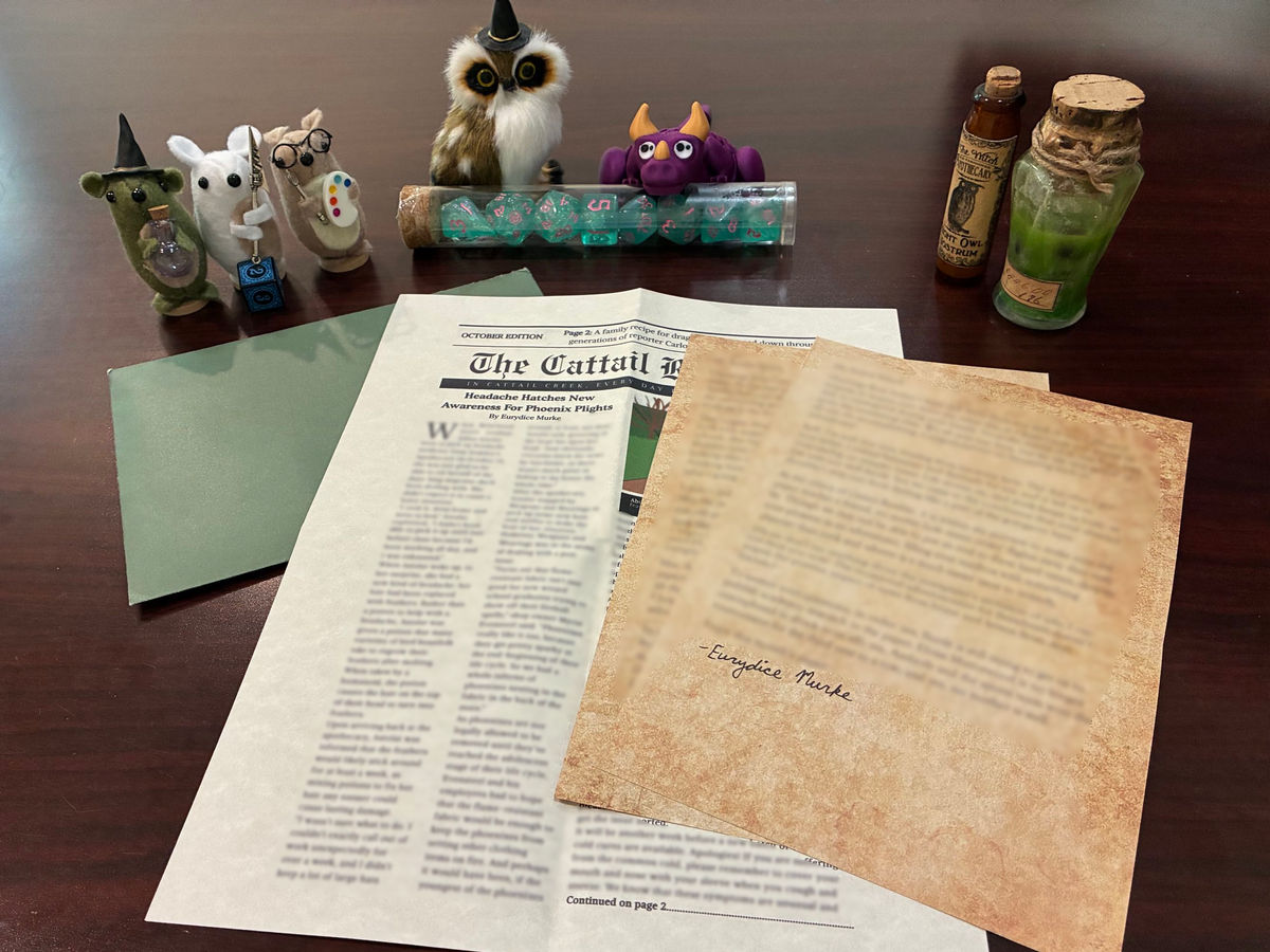A tabletop display of fantasy-themed props and d12 printed materials on a dark wood surface, including small figurines, bottles, and dice, as a background. In the foreground are d12 elements: a green envelope, d12's newspaper, and two letters on what looks like aged parchment sheets.